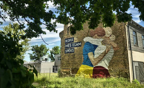 In a mural on a building in Riga, two women, depicted in Ukrainian and Latvian colors, embrace next to the phrase, "Together we are strong."